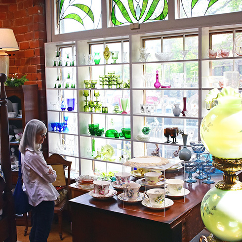 Woman viewing antique glass and china items inside antique store